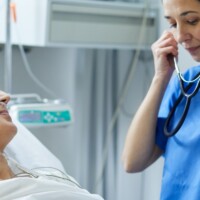 An ICU nurse is putting the stethoscope on her ears to examine a patient.